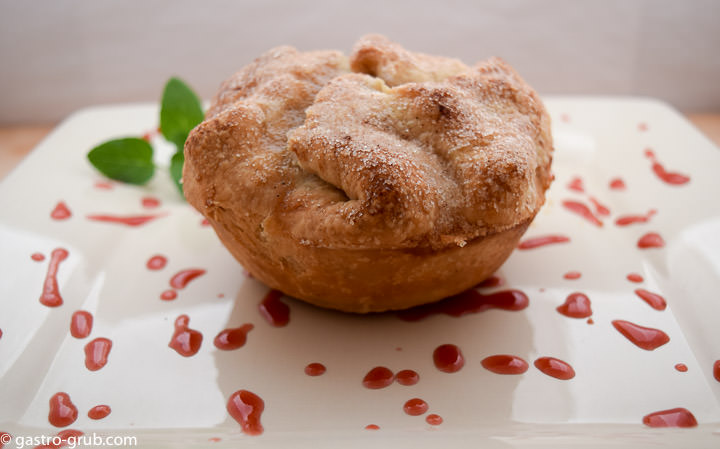 Individual apple pie on a plate with strawberry coulis.
