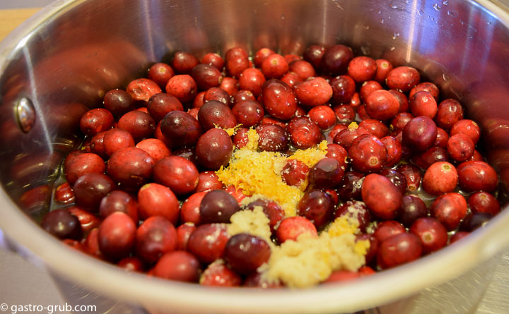 Cranberries in a pot with water, orange juice, orange zest, ginger, sugar, and salt.