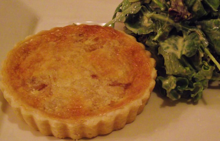 Onion and bacon tart on a plate with a green salad.