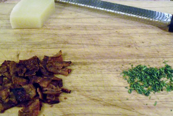 Bacon pieces, thyme, and cheese on a cutting board.