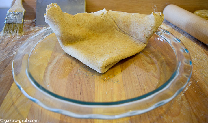 Pie dough being transferred to a pie plate, by folding it into fourths.