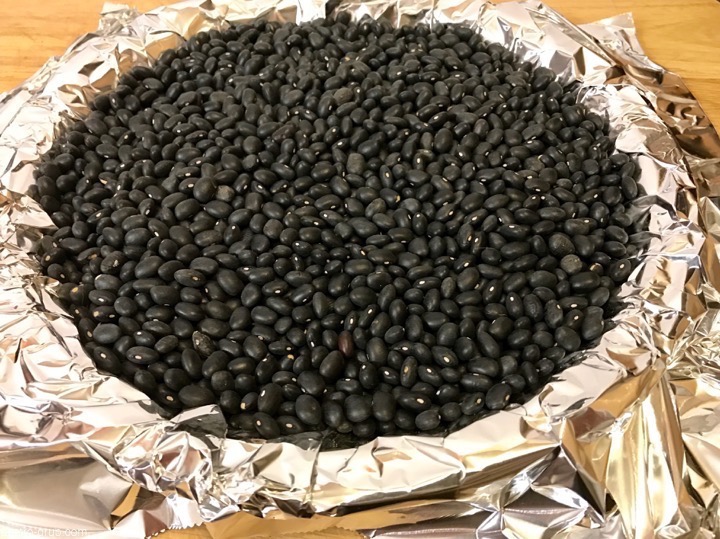 Pie crust lined with foil and filled with black beans for blind baking.