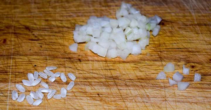 Diced onions for risotto alongside arborio rice grains.