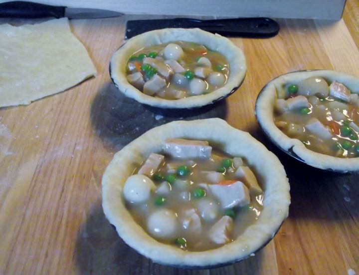 Pot pies being filled with chicken, vegetables, and sauce.