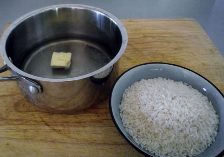 Ingredients for white rice: water, butter, and salt in a sauce-pan and white rice in a bowl.