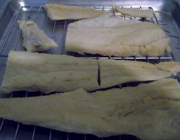 Salt cod drying on a rack over a sheet pan.