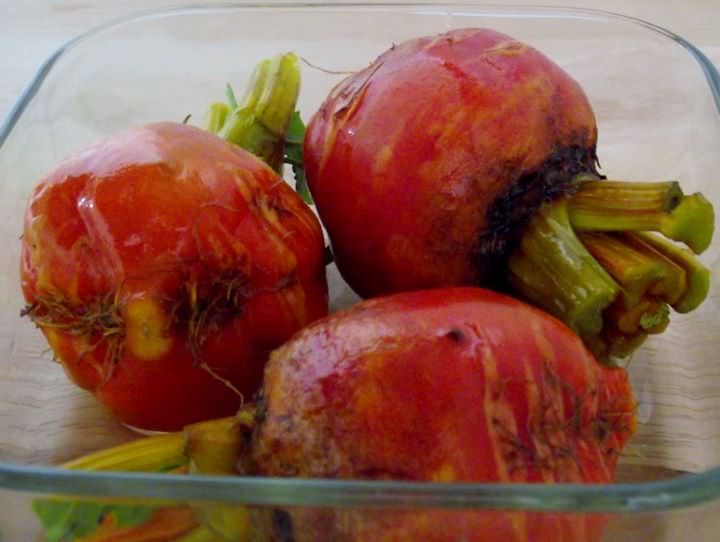 Golden beets and olive oil in a glass roasting dish.