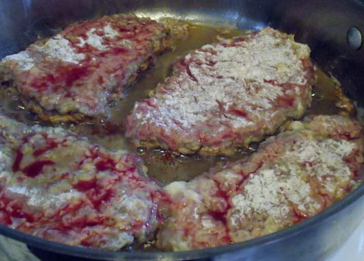 Breaded steaks frying in a saute pan.