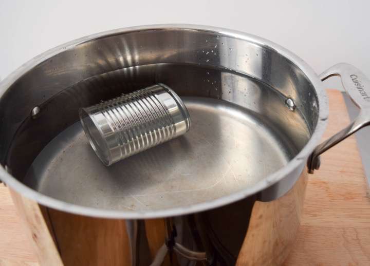 A pot with a can of sweetened condensed milk submerged in water.