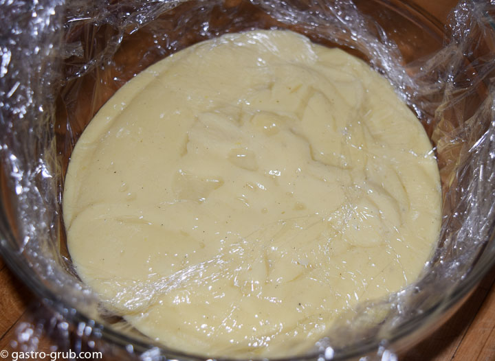 Pastry cream in a bowl with plastic wrap over the surface.