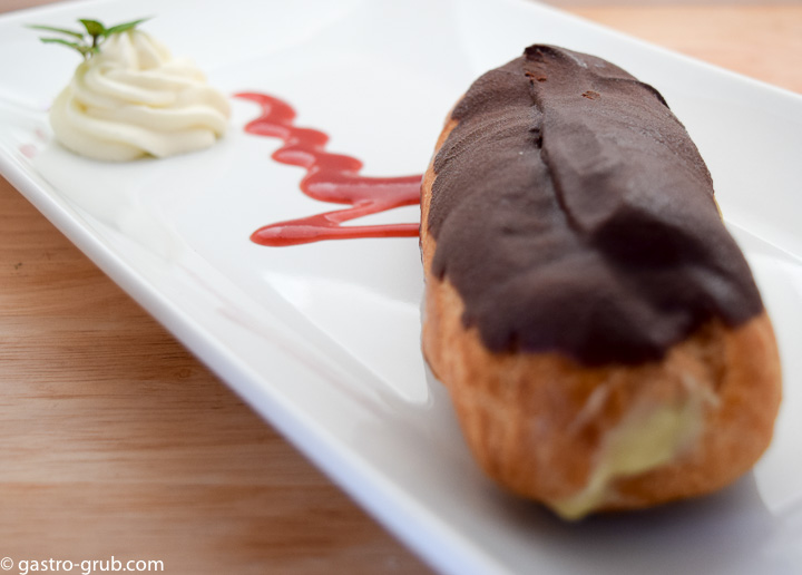 Chocolate eclair on a plate with strawberry coulis and whip cream.