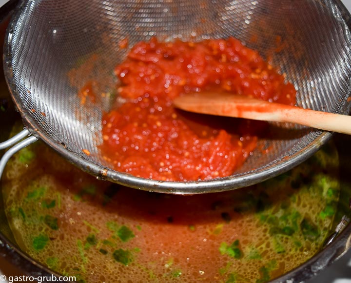 Stirring the tomatoes through a mesh strainer to break them up.
