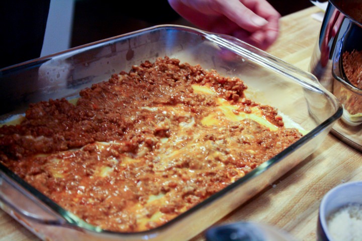 Building the lasagna by layering with sauce, pasta and cheese.