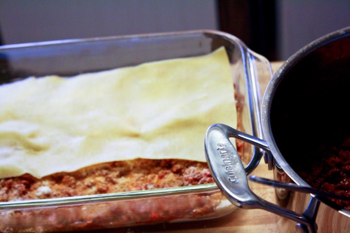 Building the lasagna by layering with sauce, pasta and cheese.