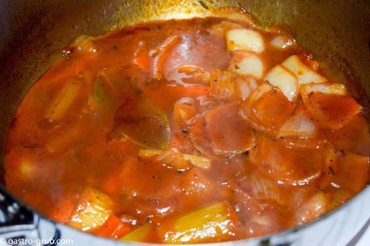 Mire poix, white wine and tomato puree reducing in a pot.