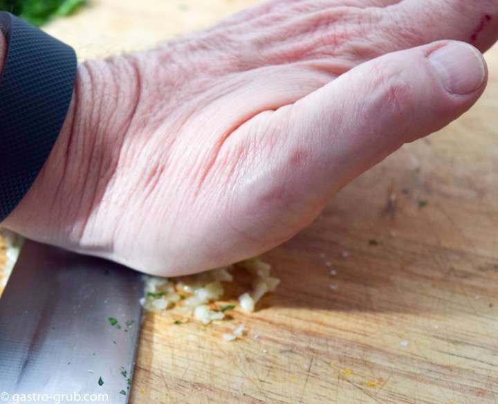 Using the flat side of the knife blade to make garlic paste.