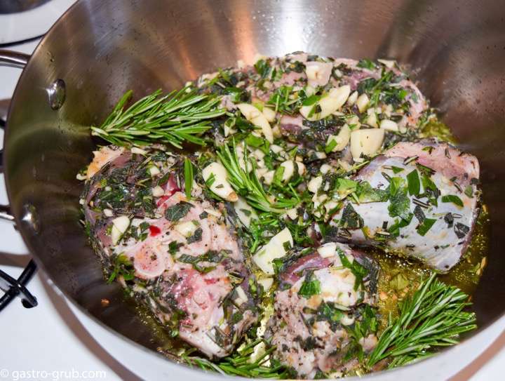 Lamb shanks browning in a pot along with herbs and garlic.