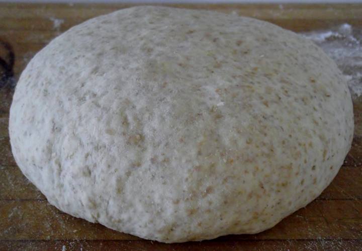 Pizza dough boule resting on a cutting board.