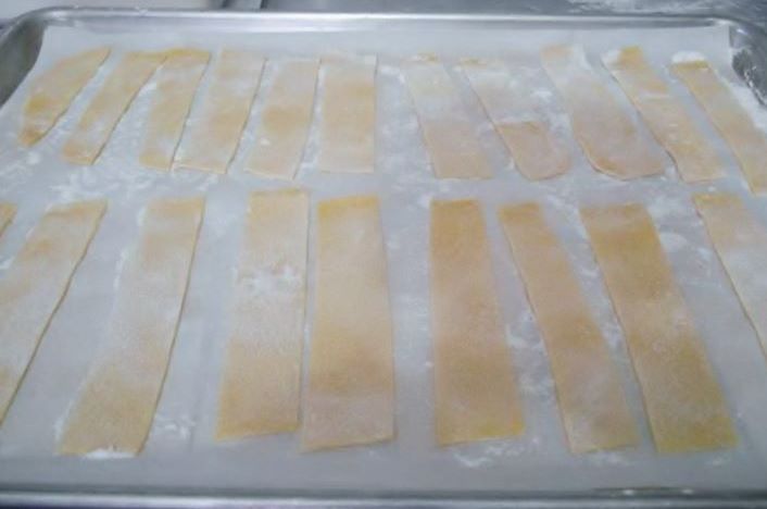 Papperdelle pasta on a parchment covered sheet pan.