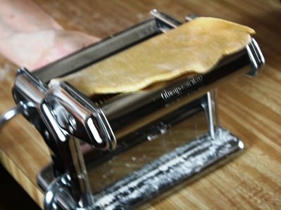 Rolling pasta dough through a pasta machine.