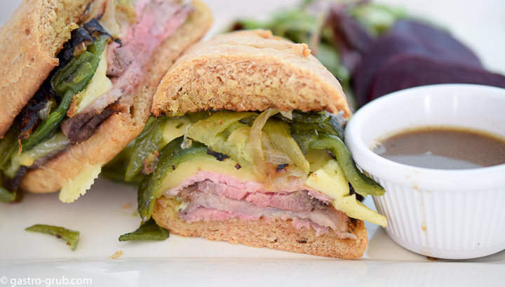 Roast beef sandwich, au jus, and green salad on a plate.