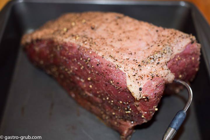Seasoned roast in a pan with a probe thermometer.
