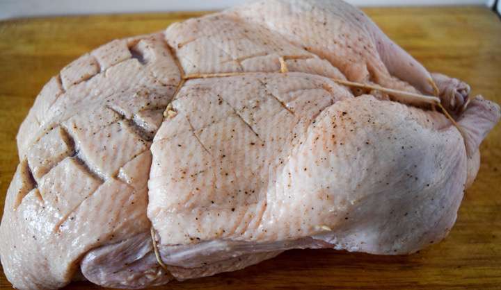 Seasoned and trussed duck on a cutting board.