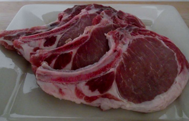 Four raw brined pork chops on a plate.