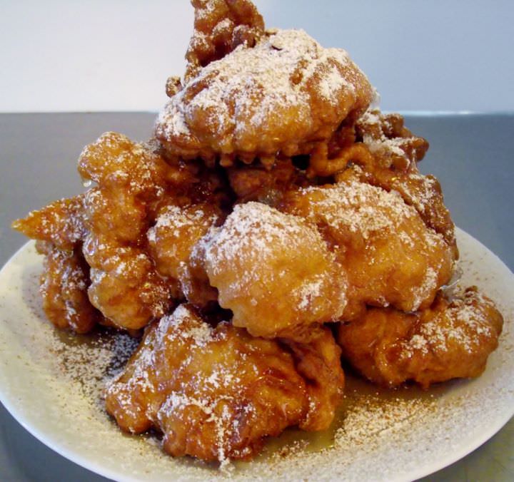 Sfinge or zeppole di San Giuseppe stacked on a plate with honey, cinnamon, and powdered sugar.