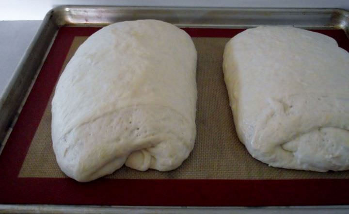 Sourdough bread loaves proofing on a sheet pan.