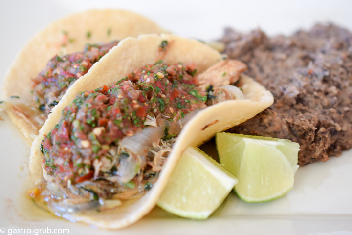 Tacos, lime wedges, and refried beans on a plate.