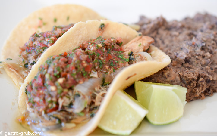 Tacos, lime wedges, and refried beans on a plate.