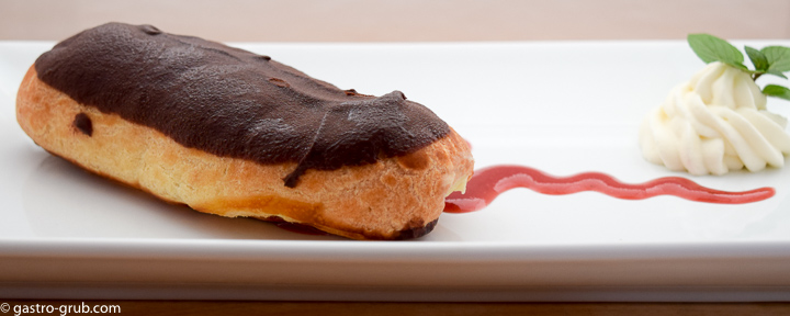 Chocolate eclair on a plate with with strawberry coulis and chantilly cream.
