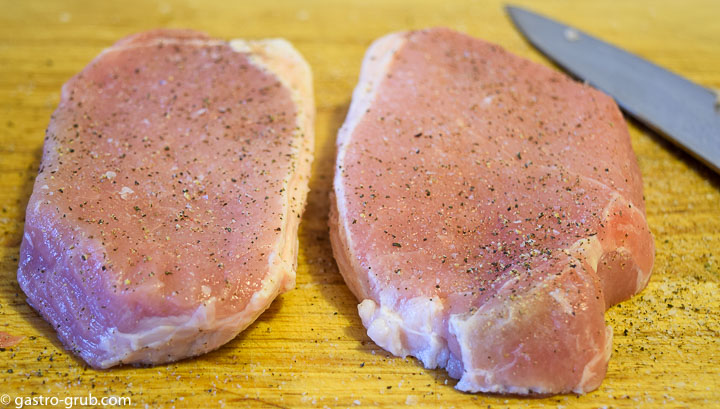Pork chops on a cutting board, seasoned with salt and pepper.